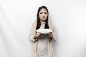 ein asiatisch Muslim Frau ist Fasten und hungrig und halten Utensilien Besteck während suchen beiseite Denken Über Was zu Essen foto