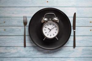 Mahlzeit Planung zum Diät Konzept, wechselnd Fasten Konzept mit Uhr auf Platte, Gabel und Messer auf hölzern Tisch, Uhr auf Teller mit Gabel und Messer, wechselnd Fasten, Mahlzeit planen, Gewicht Verlust foto