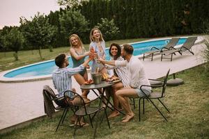 Gruppe junger Leute, die mit Apfelwein am Pool im Garten jubeln foto