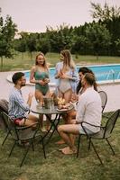 Gruppe junger Leute, die mit Apfelwein am Pool im Garten jubeln foto