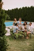 Gruppe junger Leute, die mit Apfelwein am Pool im Garten jubeln foto