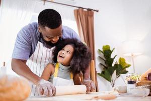 glücklicher afroamerikanischer vater und tochter, die spaß haben, während sie zu hause plätzchenteig zubereiten. glückliche Familienzeit. foto