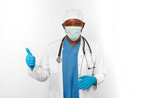 schwarz der Chirurg Arzt Mann im Weiß Mantel Handschuhe Weiß Deckel und der Chirurg Maske macht Daumen oben Geste foto