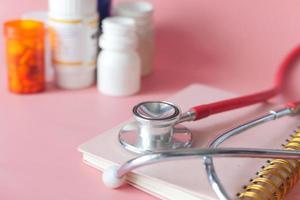 Stethoskop und Pillenbehälter auf rosa Hintergrund foto