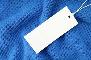 Weiß rechteckig Kleidung Etikett auf Blau gestrickt Stoff Hintergrund. Einkaufen, Verkauf, Rabatt Attrappe, Lehrmodell, Simulation foto