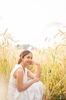 jung asiatisch Frauen im Weiß Kleider Sitzung im das Gerste Reis Feld foto