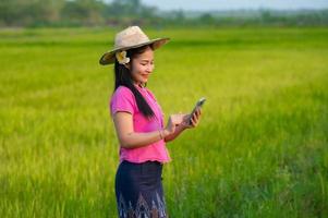 asiatisch weiblich Farmer halten Tablette Gehen im Reis Feld zu Geschäft Information foto