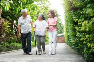 glücklich Familie Gehen zusammen im das Garten. alt Alten mit ein Gehen Stock zu Hilfe gehen Gleichgewicht. Konzept von Liebe und Pflege von das Familie und Gesundheit Versicherung zum Familie foto