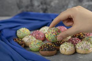Frauenhand, die einen bunten süßen kleinen Donut mit Streuseln nimmt