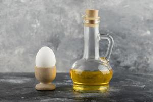 eine hölzerne Eierschale mit gekochtem Hühnerei und einer Glasflasche Öl