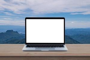moderner Laptop-Computer mit leerem Bildschirm auf Holztisch über Berg- und Himmelshintergrund. foto