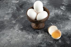 Schüssel mit weißen Eiern und einem zerbrochenen Ei auf einem Marmorhintergrund