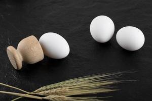 Eier, Weizen und ein hölzerner Eierbehälter auf einem schwarzen Hintergrund foto