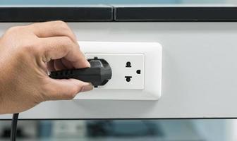 Hand, die einen Stecker aus einer Steckdose zieht foto