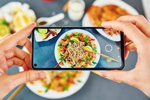 nehmen Foto von rühren braten Nudel mit Smartphone zum Sozial Medien