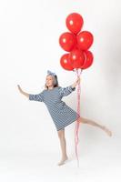 glücklich Mädchen halten groß Bündel rot Luftballons im Hand, lächelnd suchen beim Kamera, Stehen auf einer Bein foto