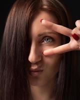 Nahansicht Porträt Frau zeigen Sieg oder Frieden Geste mit Finger in der Nähe von Auge und suchen beim Kamera foto