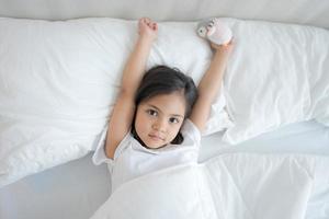 das wenig Mädchen aufwachen oben im ein komfortabel Weiß Schlafzimmer. foto