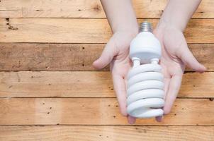 Energie Speichern Konzept, Frau Hand halten Licht Birne auf hölzern Hintergrund, Ideen Licht Birne im das Hand foto