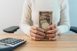 Frauenhand, die japanische Yen-Banknote mit Taschenrechner zählt. Tausend Yen Geld. japan bargeld, steuer, rezessionswirtschaft, inflation, investition, finanzen, einsparungen, gehalts- und zahlungskonzepte foto