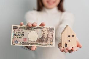 Frau mit japanischer Yen-Banknote und Hausmodell. immobilien, haus, hypothek, japanisches bargeld, steuer, rezessionswirtschaft, inflation, investition, finanz- und sparkonzepte foto