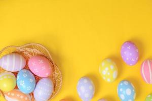 glücklich Ostern Feier Urlaub. bunt Pastell- gemalt Eier im Korbweide Korb Nest Dekoration auf ein Gelb Hintergrund. saisonal Gruß Geschenk Karte Konzept. oben Sicht, eben legen, Kopieren Raum. foto