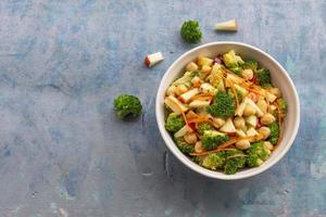 gesund Essen Brokkoli Salat hinzufügen Apfel Kichererbsen im Weiß Schüssel auf Blau Holz Hintergrund. foto