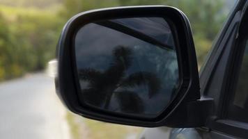 abstrakt von Spiegel Flügel von dunkel Auto mit Betrachtung von dunkel Bäume verwischen im Spiegel. verschwommen Hintergrund von Asphalt Straße und Grün Baum. foto