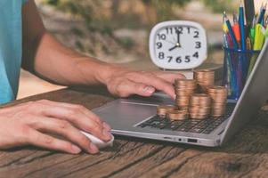 Eine Person, die einen Computer mit einem Stapel Münzen benutzt, verdient Geld online Konzept foto