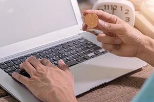 Eine Person, die einen Computer mit einer Münze benutzt, verdient online Geld foto
