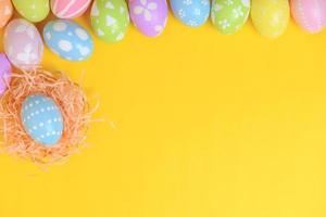 glücklich Ostern Feier Urlaub. bunt Pastell- gemalt Eier im Korbweide Korb Nest Dekoration auf ein Gelb Hintergrund. saisonal Gruß Geschenk Karte Konzept. oben Sicht, eben legen, Kopieren Raum.