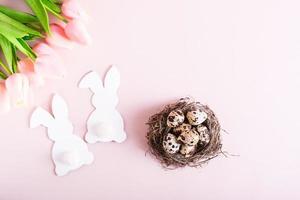 glücklich Ostern Paar von Weiß Kaninchen, Wachtel Eier im Nest und Blumen auf Rosa Hintergrund oben Aussicht foto