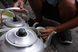 Gießen warm Tee Wasser im ein Weiß Tasse während Dorf Aufräumen Arbeit foto