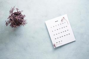 leer Blatt von das monatlich Kalender und ein Strauß von getrocknet Blumen auf das Tisch. Zeit Planung und Organisation foto