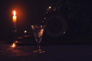 Glas mit Weiß Wein mit Jahrgang alt hölzern Uhr und Verbrennung Gelb Kerze Girlande Beleuchtung auf das Hintergrund. Mitternacht auf Uhr. Nacht festlich Bild zum Hintergrund. schön golden Beleuchtung. foto