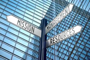 Mission, Management, Ressourcen - - Wegweiser mit drei Pfeile, Büro Gebäude im Hintergrund foto