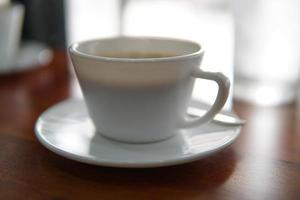 ein Becher von heiß schwarz Kaffee steht auf ein hölzern Tisch. Weiß Becher mit Kaffee foto