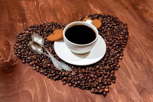 weiße Kaffeetasse, herzförmiger Lebkuchen und zwei Löffel auf einem Herzen foto