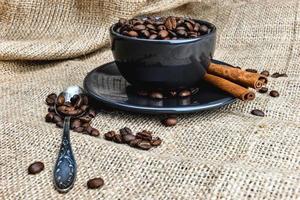 schwarze Kaffeetasse voller Bio-Kaffeebohnen und Zimtstangen auf Leinentuch foto