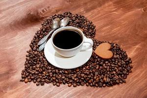 weiße Kaffeetasse, herzförmiger Lebkuchen und zwei Löffel auf einem Herzen foto