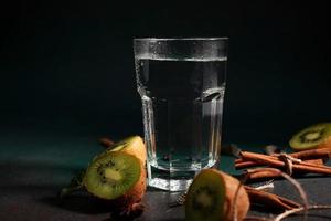 ein Glas von kalt Wasser auf ein Grün Hintergrund. dekoriert mit Scheibe Kiwi, Zimt Stöcke, badyan, Minze Blätter. Kopieren Raum foto