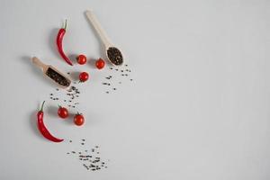 Kirsche Tomaten, rot heiß Chili Pfeffer, duftend schwarz Pfeffer Erbsen auf ein Weiß Hintergrund. Hintergrund mit Gewürze. eben legen, oben Aussicht und Kopieren Raum foto