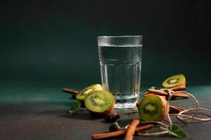 ein Glas von kalt Wasser auf ein Grün Hintergrund. dekoriert mit Scheibe Kiwi, Zimt Stöcke, badyan, Minze Blätter. Kopieren Raum foto