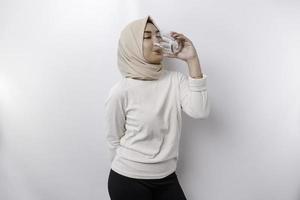 froh asiatisch Muslim Frau tragen Kopftuch ist Trinken ein Glas von Wasser, isoliert auf Weiß Hintergrund. foto