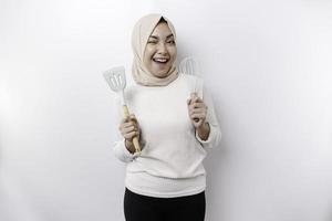 aufgeregt asiatisch Muslim Frau tragen ein Kopftuch, halten Kochen Ware und lächelnd, isoliert durch Weiß Hintergrund foto