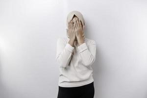 jung asiatisch Muslim Frau isoliert auf Weiß Hintergrund, sieht aus deprimiert, Gesicht bedeckt durch Waffen erschrocken und nervös. foto