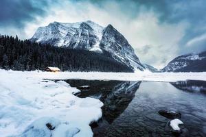 Landschaft von See Louise mit hölzern Hütte glühend und felsig Berge mit Schnee bedeckt im Winter beim banff National Park foto