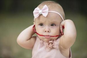 das komisch Mädchen dauerte ein rot Band im ihr Mund. einer Jahr alt Kind. ein süß Baby. foto