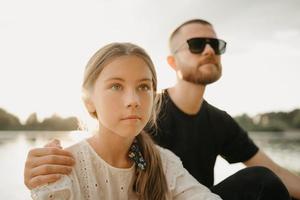 ein enges Porträt eines jungen Mädchens, das mit ihrem Vater mit einem Bart posiert, der sie umarmt foto