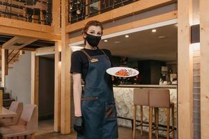 Eine Kellnerin, die eine schwarze Gesichtsmaske trägt, hält einen Minz-Dolendwitz-Salat in der Hand foto